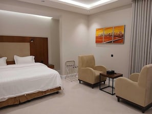 A hotel room with a bed, two armchairs, a small table, and a wall-mounted painting. - Raoum Inn Shaqra (Shaqra)