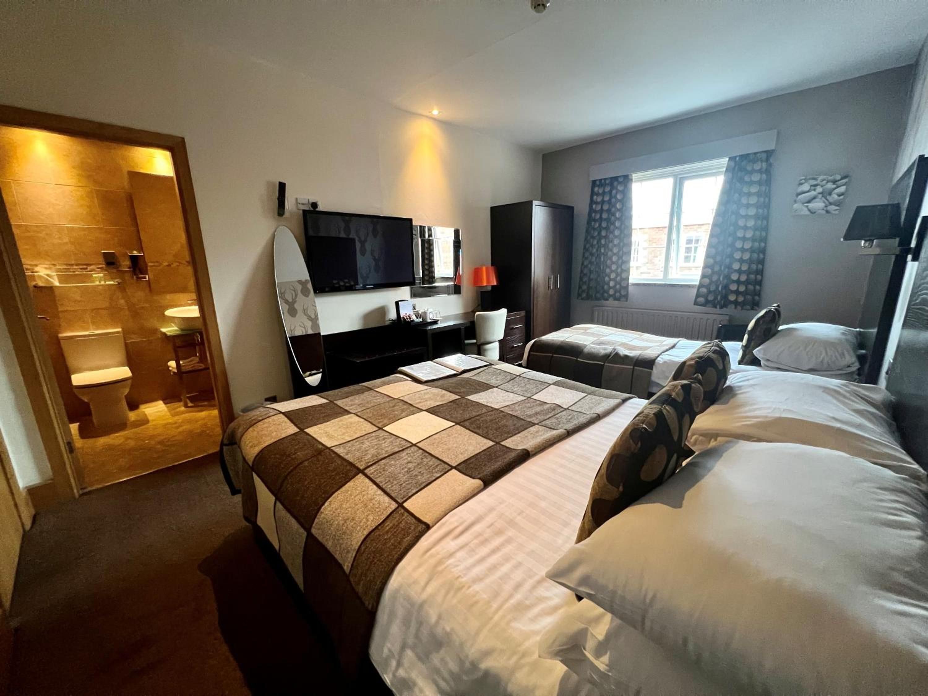 A hotel room with two beds, a TV, a desk, and a bathroom visible through an open door.