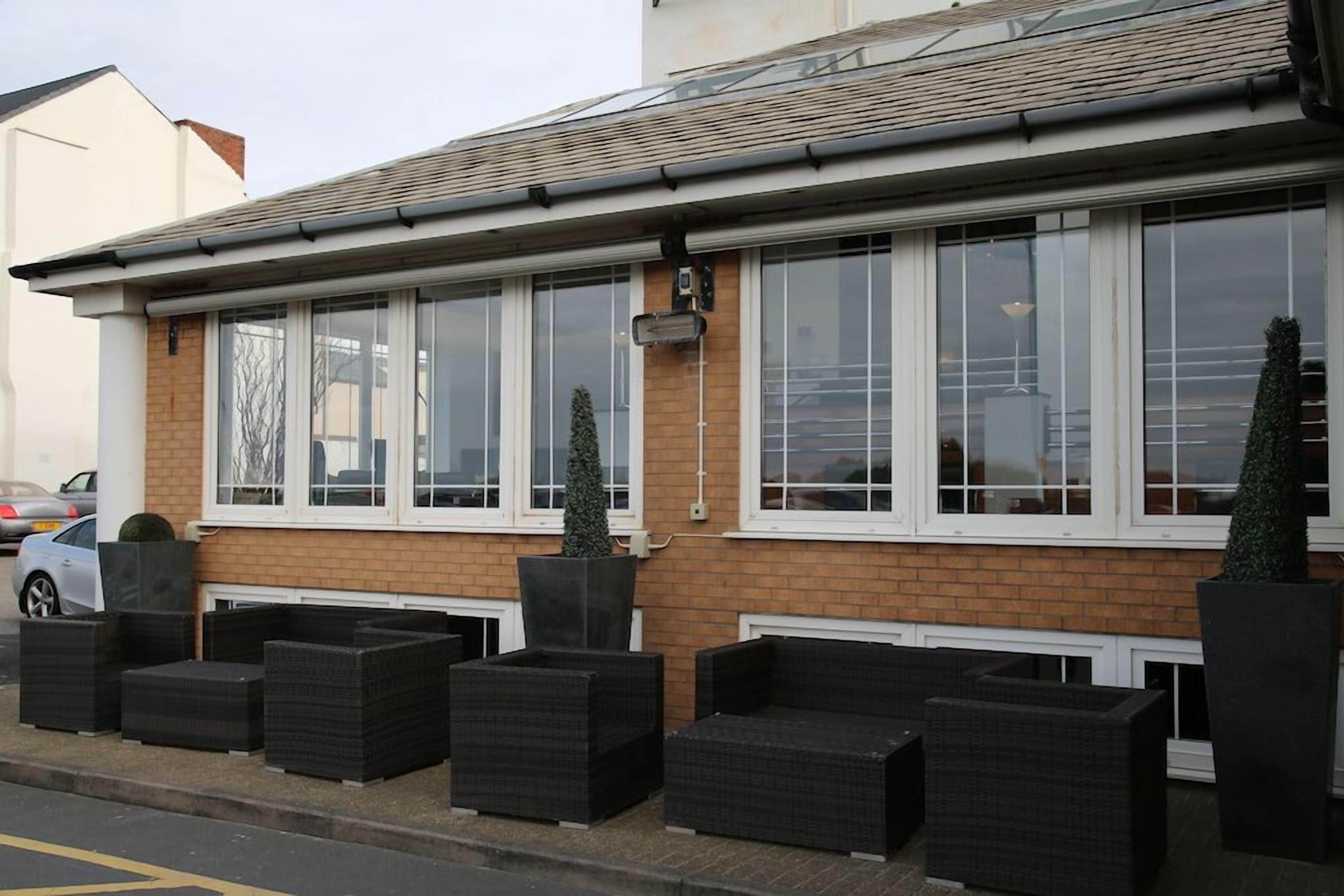 A two-story building with a brick facade, large windows, and outdoor seating with black wicker furniture.