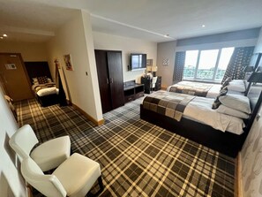A hotel room with a checkered carpet, two beds, a desk, a chair, and a television.