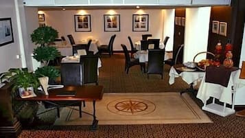 A hotel lobby with a carpeted floor, tables, chairs, and a large decorative rug.