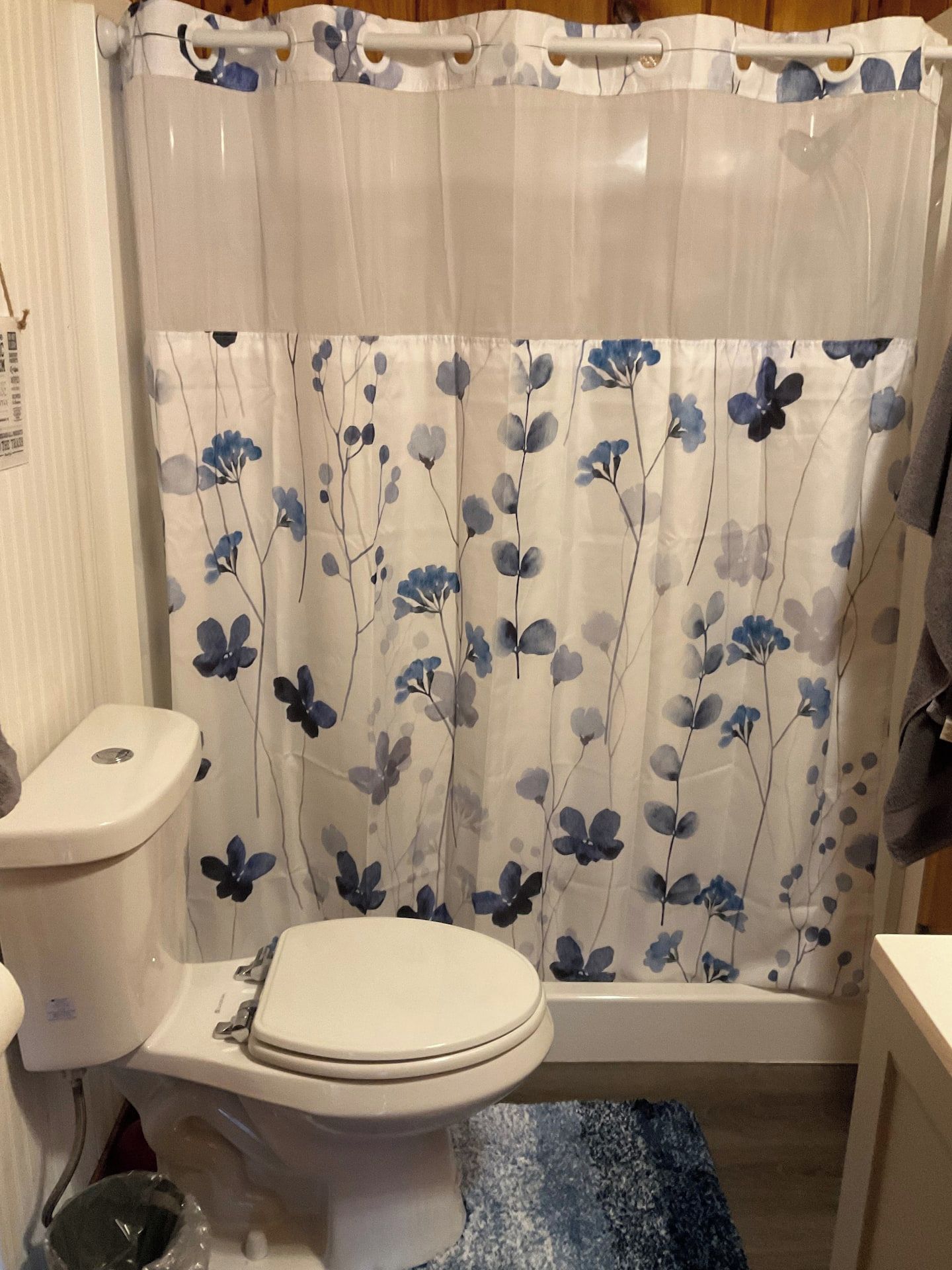 Un baño con inodoro, cortina de ducha con estampado floral y alfombra azul con textura.