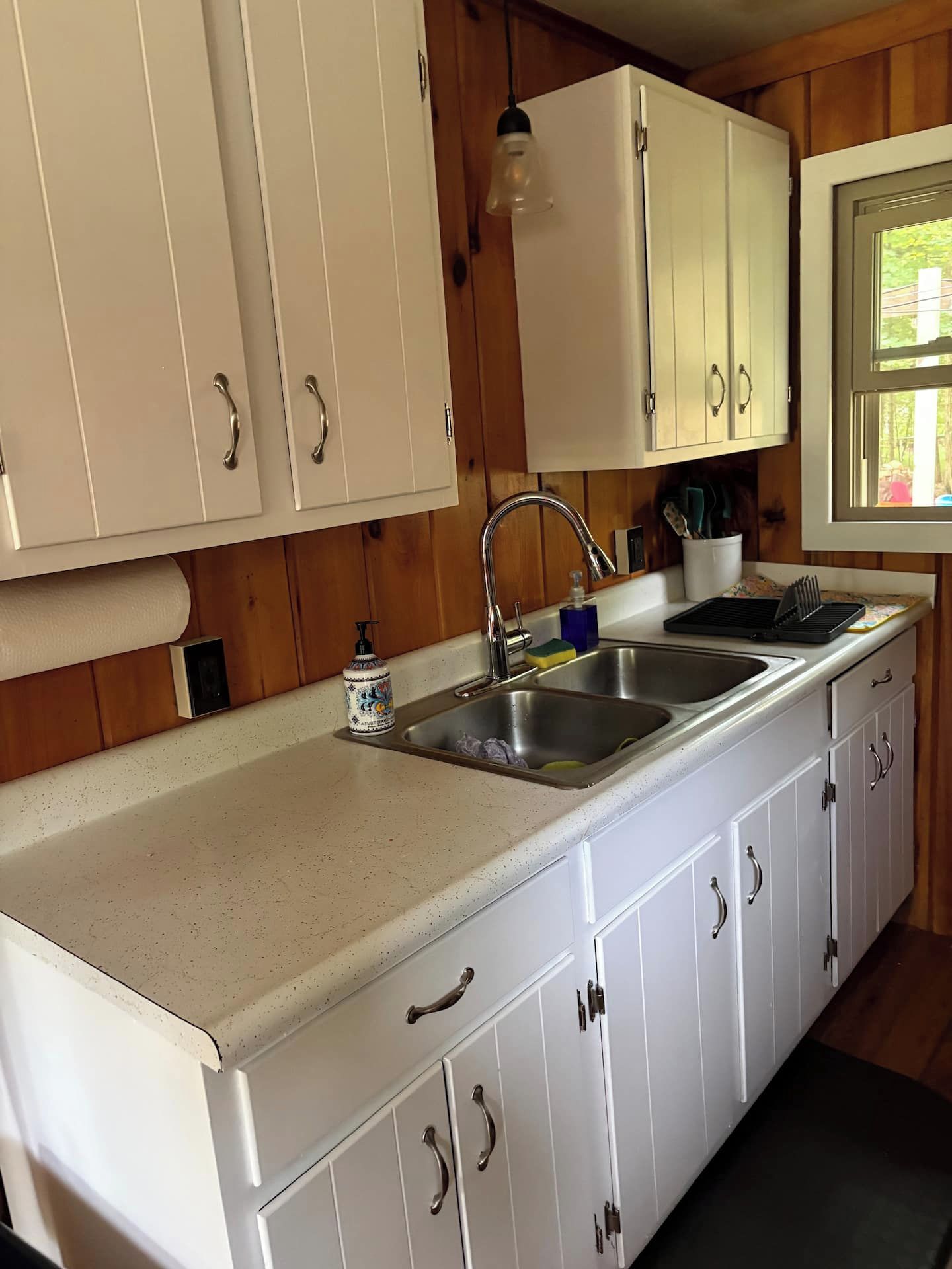 Una cocina con armarios blancos, un lavamanos de acero inoxidable y paneles de madera.