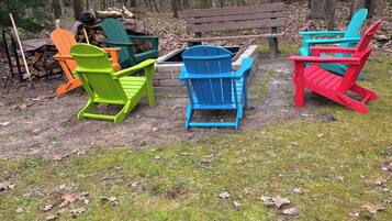 Un área boscosa con un banco de madera y sillas Adirondack de colores.