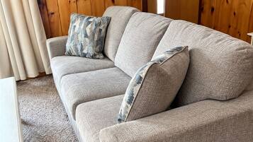 Ein graues Sofa mit gemusterten Kissen, ein weißer Tisch und eine Holzwand mit einer Flagge.