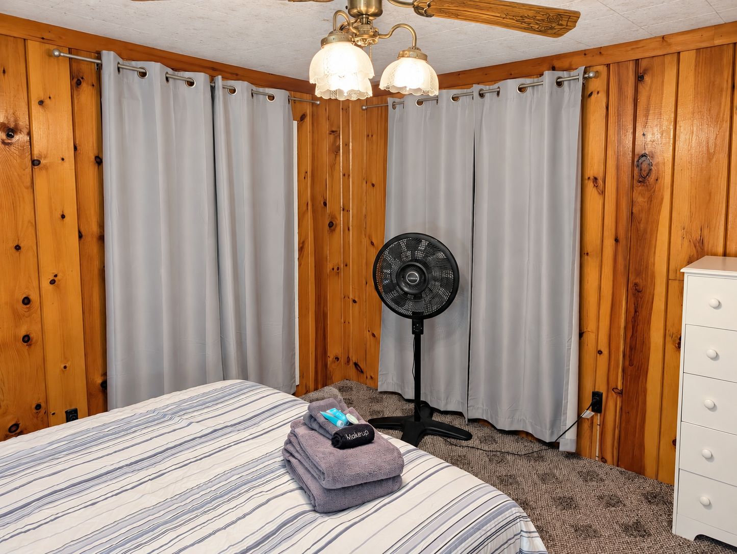 Een hotelkamer met een bed, een ventilator en houten wanden.