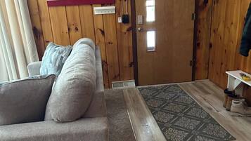 A room with a wooden wall, a sofa, a rug, and a door with windows.