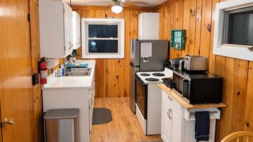 A compact kitchen with wooden walls, a window, a stove, a microwave, and a sink.