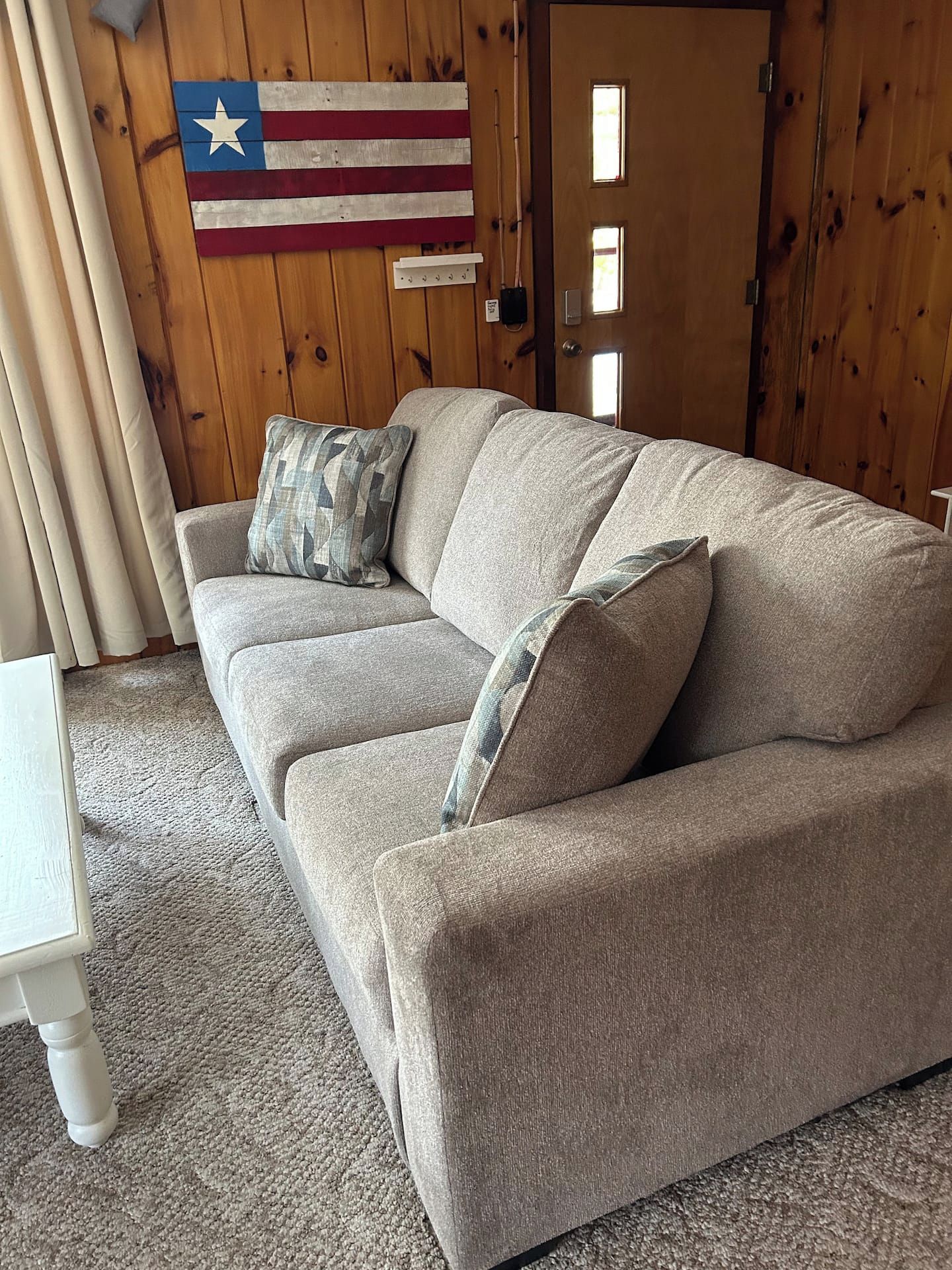 A beige sofa with two pillows in a room with wooden walls and a flag.