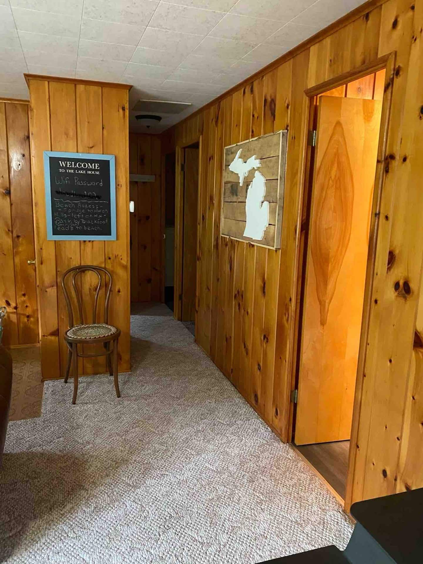 Un pasillo de madera con un cartel de bienvenida, una silla y una puerta con un diseño recortado.