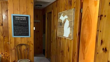 Un pasillo de madera con un cartel de bienvenida, una silla y una puerta con un diseño recortado.