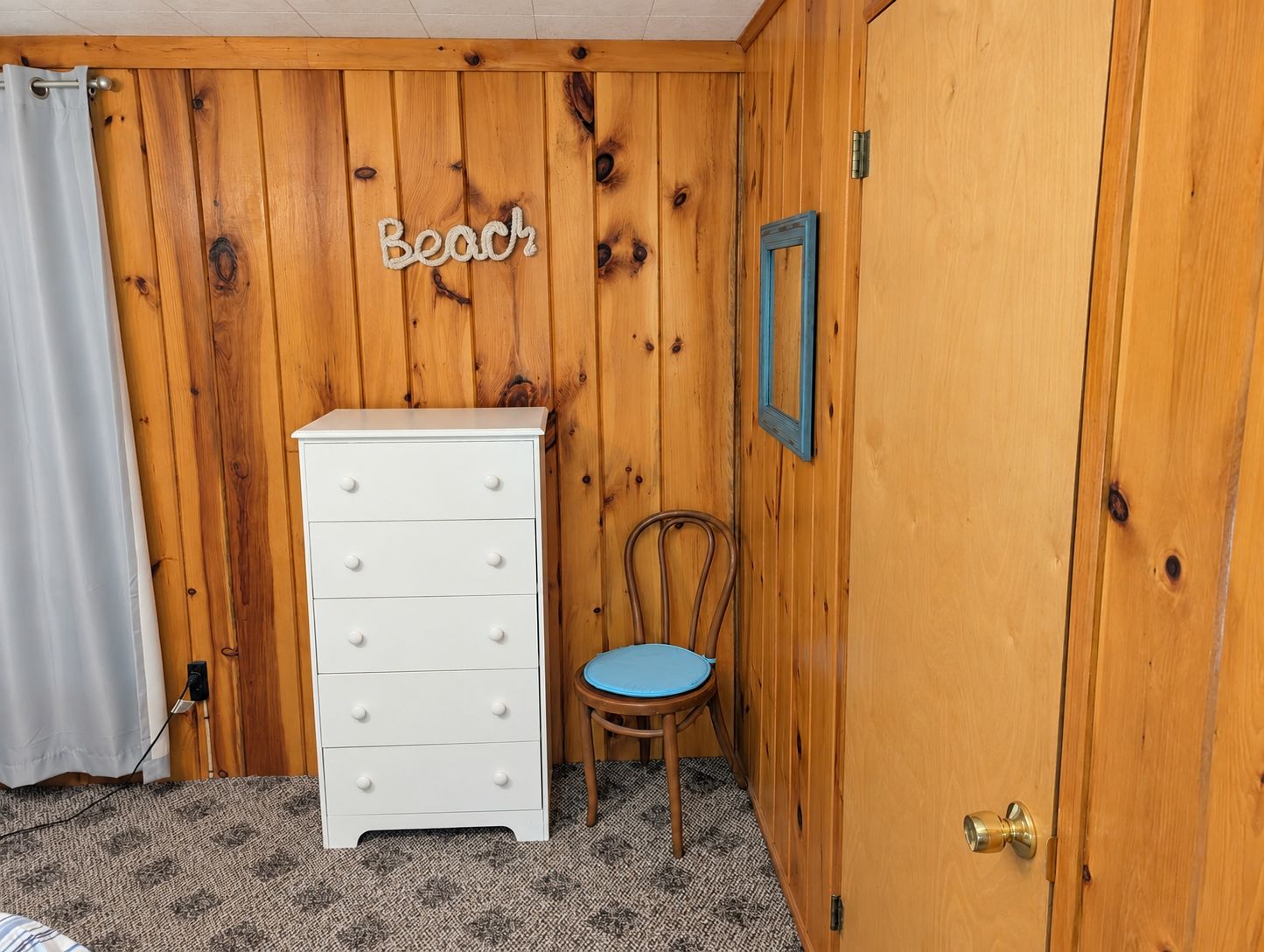 Een kamer met een houten wand, een witte dressoir, een blauwe stoel en een deur met een koperen handvat.