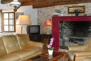 A living room with leather sofas, a television, a fireplace, and a stone wall. - Holiday home in Crozon with swimming pool (crozon)