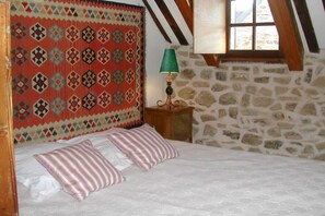 A bedroom with a stone wall, a bed with white linens, striped pillows, and a patterned headboard. - Holiday home in Crozon with swimming pool (crozon)