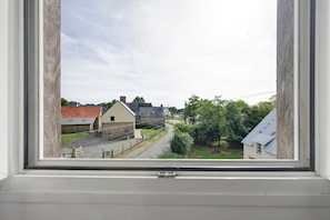 Vista a través de una ventana de una calle rural con casas, una carretera y vegetación.