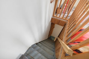 Una escalera de madera con barandilla que lleva a una habitación con cama.