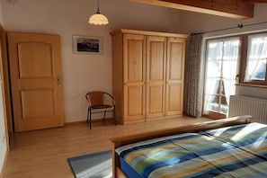 A bedroom with a bed, wooden wardrobe, a chair, and a window with curtains. - Holiday apartment with 1 bedroom (Garmisch-Partenkirchen)