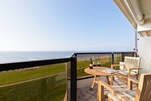 A balcony with a view of the ocean, a table with chairs, and a bottle of wine. - Holiday apartment with 1 bedroom (Norderney)
