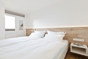 A modern bedroom with a large bed, a bedside table, and a view of the outdoors. - Holiday apartment with 1 bedroom (Norderney)
