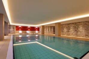 A swimming pool with a tiled floor, a stone wall, and a red wall with lights. - Holiday apartment with 1 bedroom (Norderney)