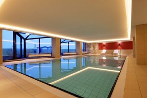 Una piscina interior con paredes de vidrio transparente, suelo de baldosas y vista al cielo.
