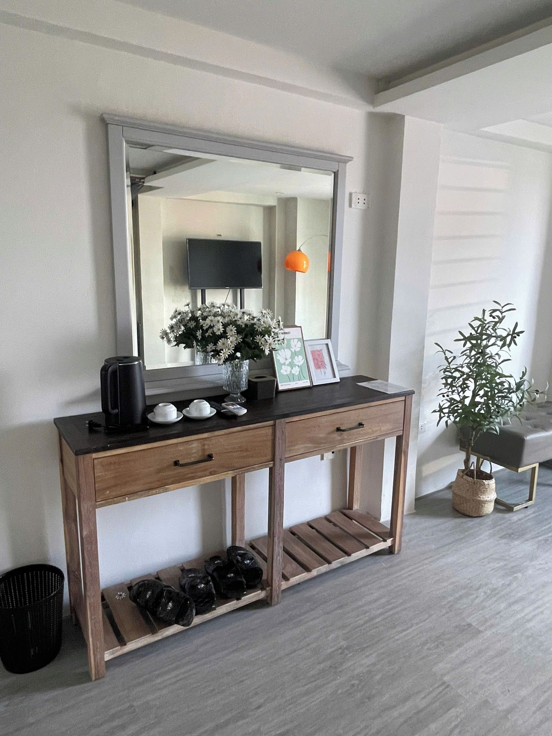Une console en bois surmontée d’un grand miroir, agrémentée d’une petite plante et d’un tableau encadré.