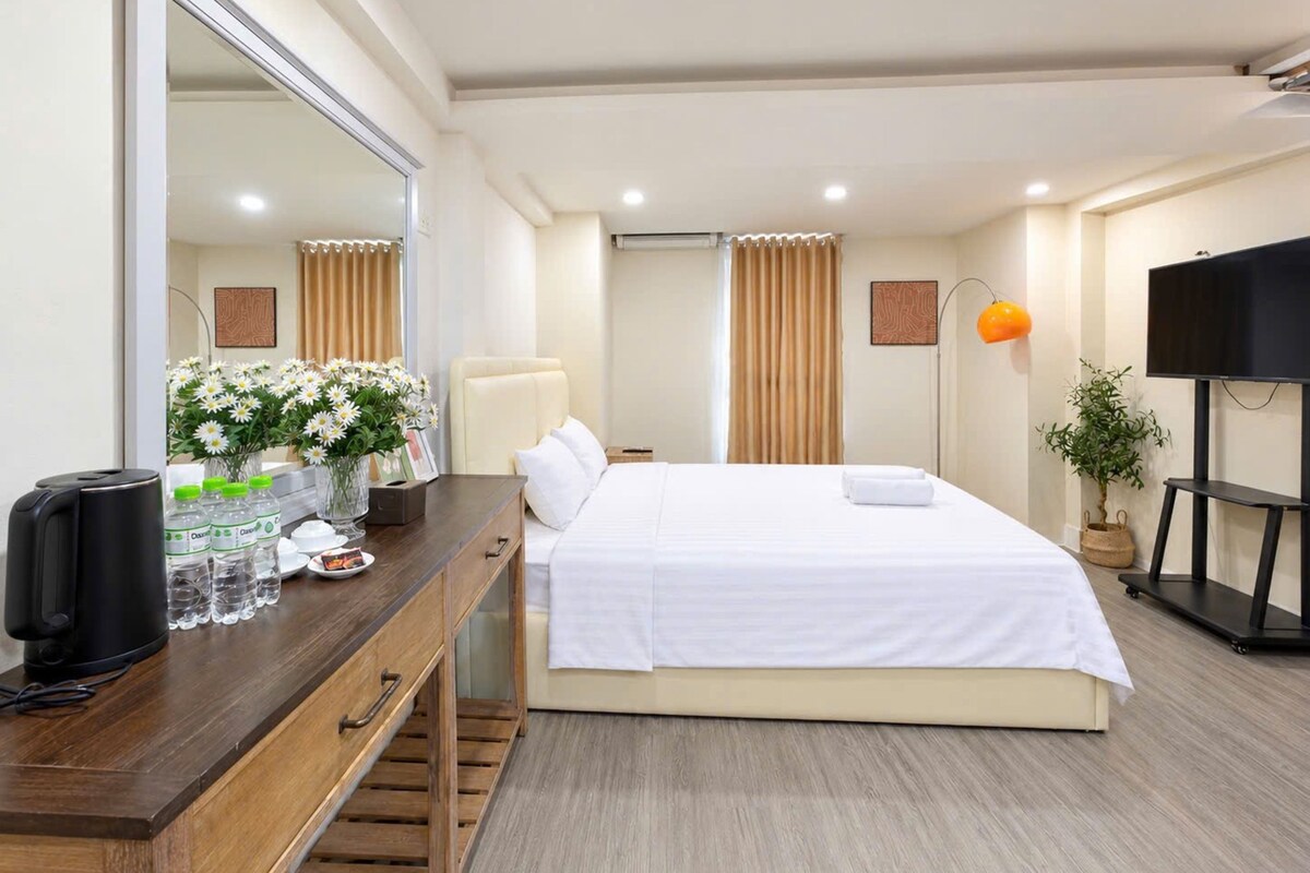 A hotel room with a bed, a wooden dresser, a mirror, a television, a lamp, and a potted plant.