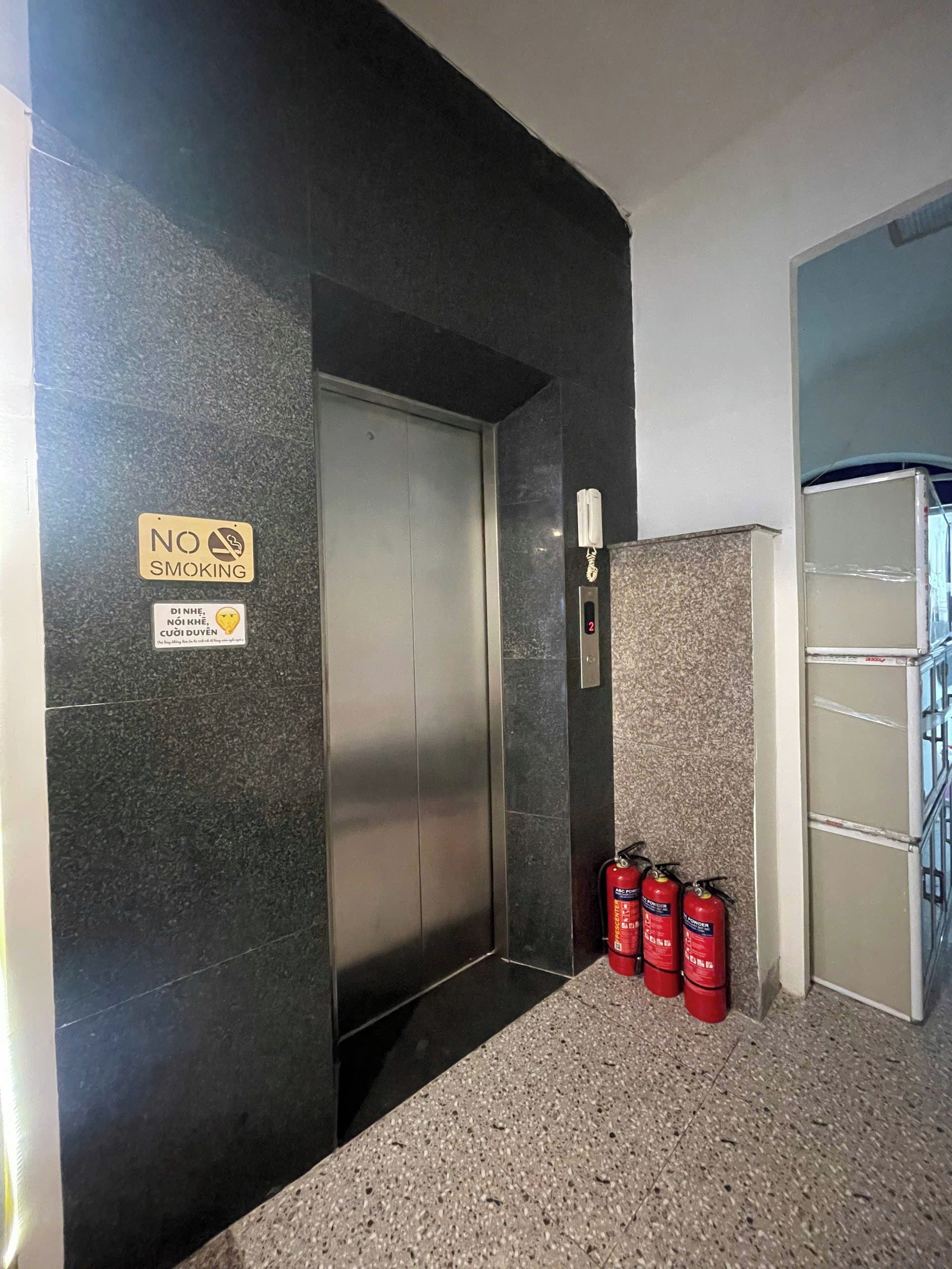 Un ascenseur sur lequel on peut lire l’inscription « INTERDICTION DE FUMER », équipé d’une alarme incendie et de deux extincteurs placés au sol.