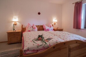 A bedroom with a wooden bed, floral bedding, bedside lamps, and a window with curtains. - Holiday apartment in Anger with swimming pool (Anger)