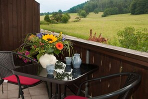 A balcony with a table, chairs, a vase of flowers, and a view of a green field. - Holiday apartment in Anger with swimming pool (Anger)