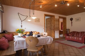 A cozy dining area with a wooden table set for a meal, a wooden chair, and a red patterned sofa. - Holiday apartment in Anger with swimming pool (Anger)