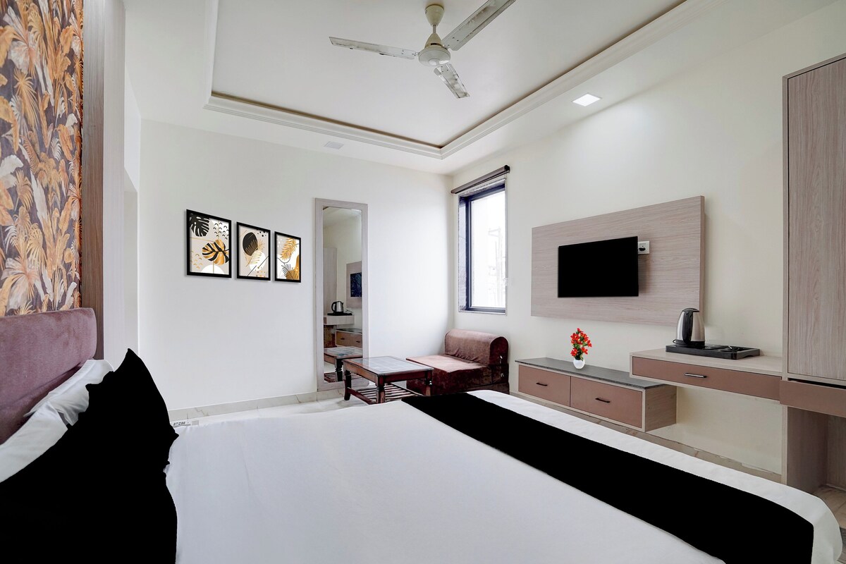 A hotel room with a bed, a desk, a chair, a television, and a ceiling fan.