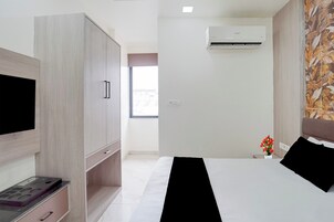 A hotel room with a bed, a wardrobe, a flat-screen TV, a small table, and an air conditioning unit.