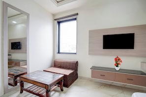 A modern living room with a glass-top coffee table, a cushioned bench, a flat-screen TV mounted on the wall, and a small potted plant. - Collection O Rudrapur Bus Terminal (Rudrapur)