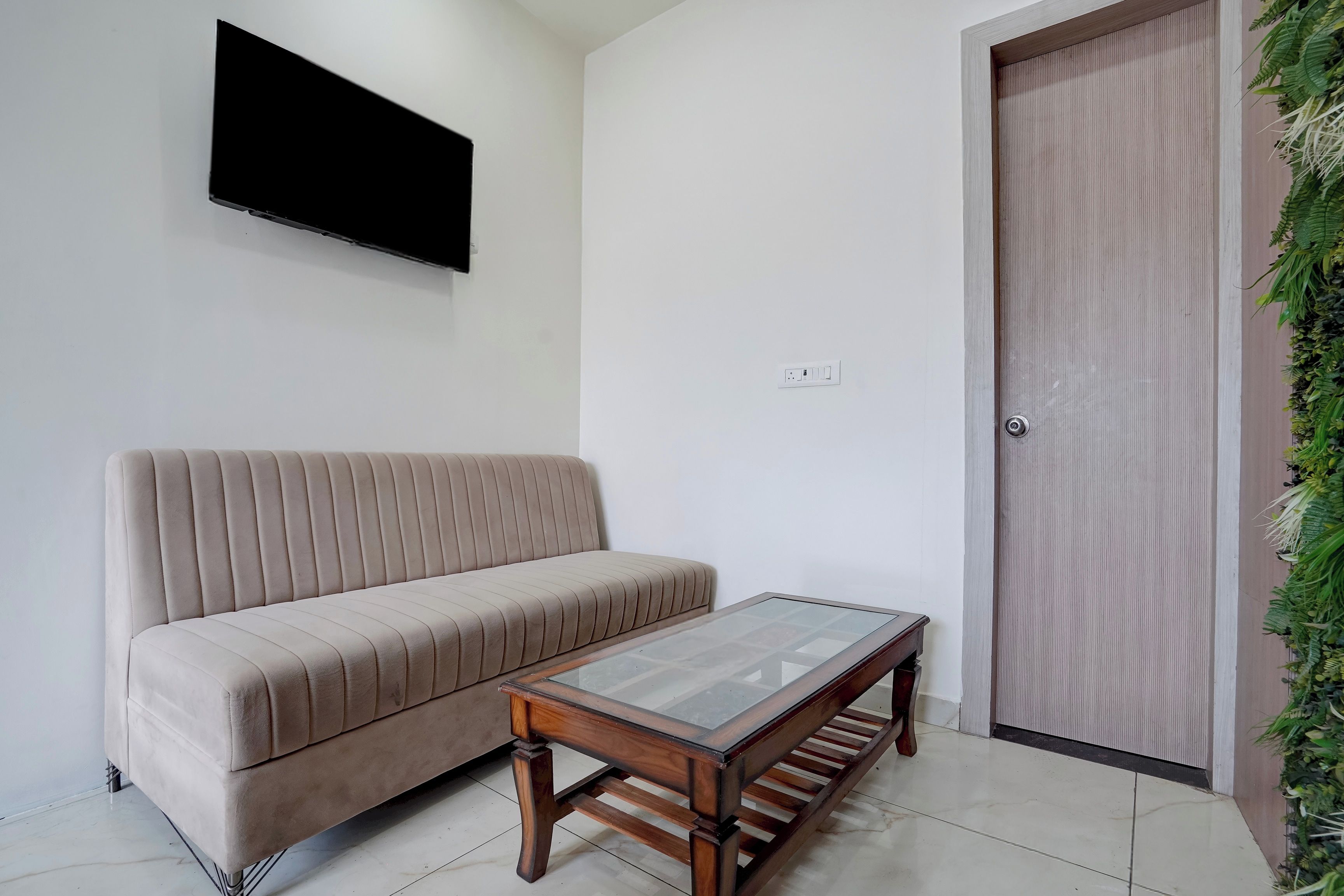 A living room with a sofa, a coffee table, a TV mounted on the wall, and a door with a vertical handle.