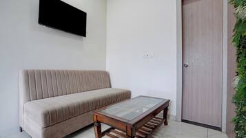 A living room with a sofa, a coffee table, a TV mounted on the wall, and a door with a vertical handle.