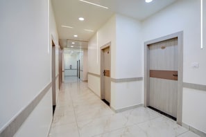 Un pasillo de hotel con piso de mármol, paredes blancas y puertas con números de habitación.