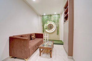 A modern living room with a brown sofa, a glass coffee table, and a decorative wall with green plants.