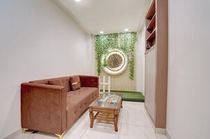 Una sala de estar moderna con un sofá marrón, una mesa de centro de vidrio y una pared decorativa con plantas verdes.