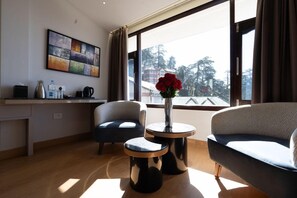A modern hotel room with a large window, a sofa, a chair, a small table with a vase of flowers, and a wall-mounted artwork. - Sterling Legacy Shimla (Shimla)