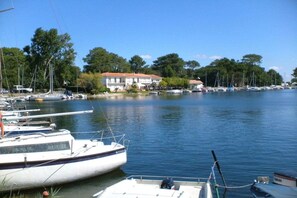 A marina with boats docked, a building with a red roof, and trees in the background. - Holiday home with 2 bedrooms (Biscarrosse)