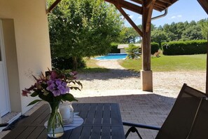 A patio with a table and chairs, a flower vase, and a view of a swimming pool and garden. - Holiday home with 2 bedrooms (Biscarrosse)