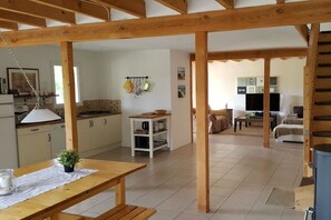 A spacious living area with a wooden ceiling structure, a kitchen with white cabinets, and a dining area with a wooden table. - Holiday home with 2 bedrooms (Biscarrosse)