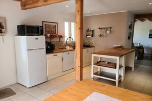 A compact kitchen with a white refrigerator, microwave, and sink. There's a wooden table and a small cart with shelves. - Holiday home with 2 bedrooms (Biscarrosse)