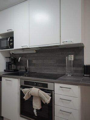 A modern kitchen with white cabinetry, a black stove, a coffee maker, and a towel hanging on the oven door. - Levi South Studio 1 and 2, Sauna By Lapland Host (Kittilä)