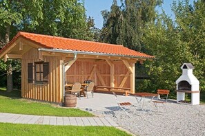 Eine hölzerne Außenkonstruktion mit einem Ziegeldach, einem Grill und einer Sitzgelegenheit mit Tischen und Stühlen.