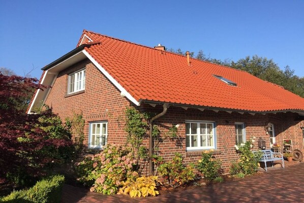A two-story brick house with a red-tiled roof, a front porch, and a small garden with various plants.