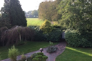 Ein angelegter Garten mit einem geschwungenen Backsteinpfad, verschiedenen Sträuchern und einem hohen Baum.