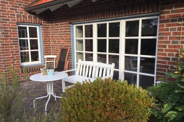 A brick building with a white bench and a table outside, a large window, and a small potted plant.