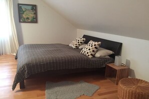 A bedroom with a bed, pillows, a nightstand, a rug, and a painting on the wall.
